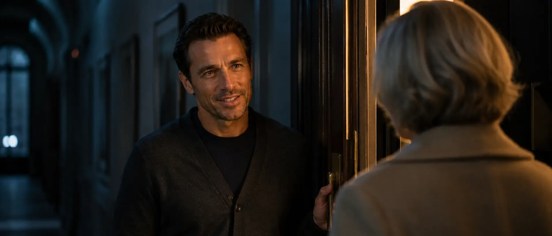Two people in quiet conversation at a lamplit doorway, evening blue all around.
